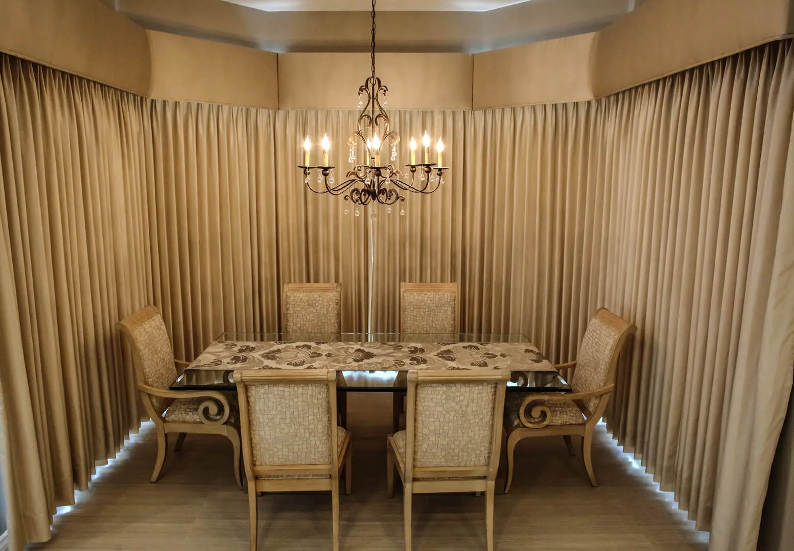 A dining room with a table and chairs, chandelier and curtains.