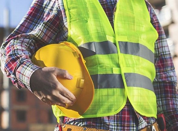 A man in yellow vest holding a hard hat.